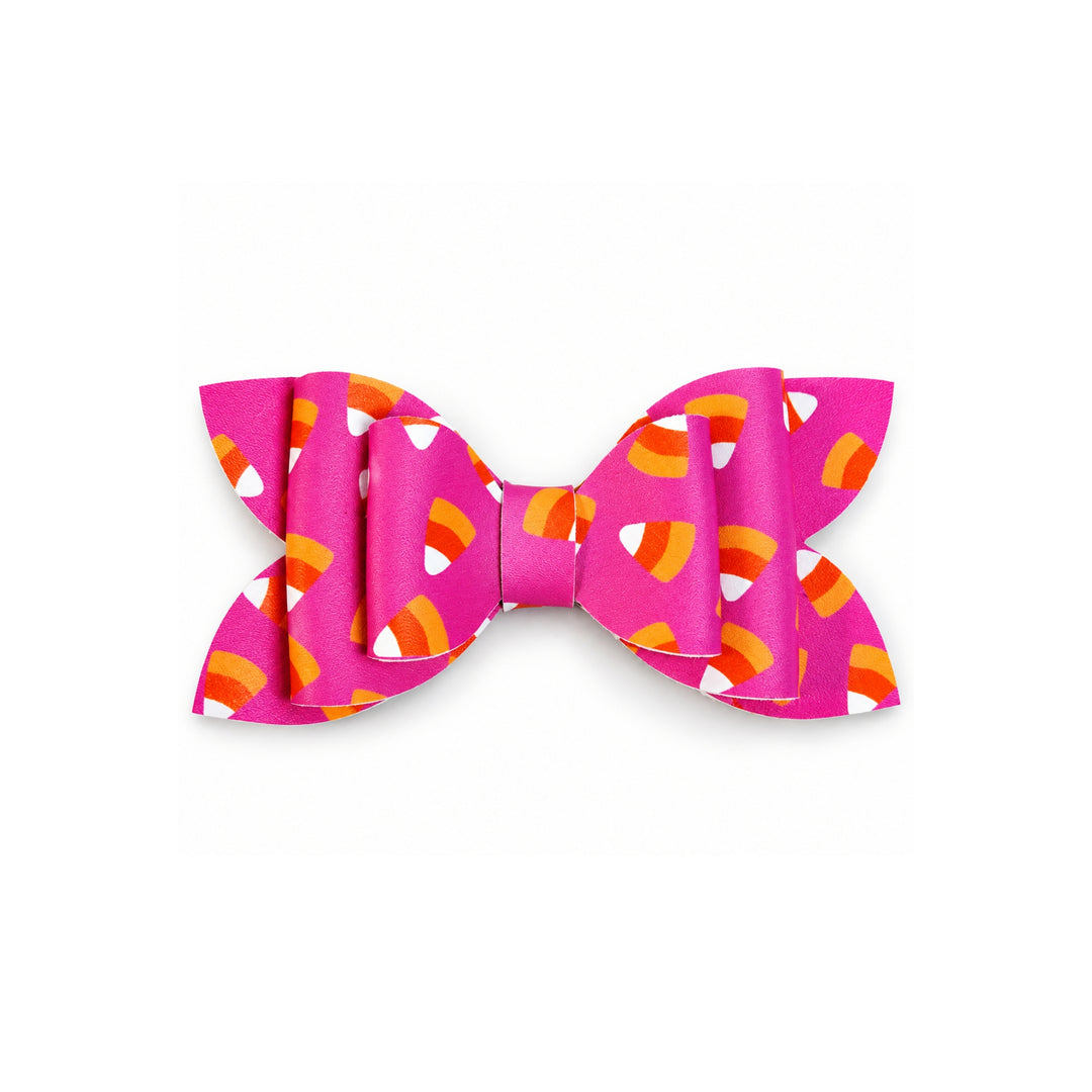 A pink bow featuring a candy corn pattern with orange, yellow, and white accents, set against a plain white background.