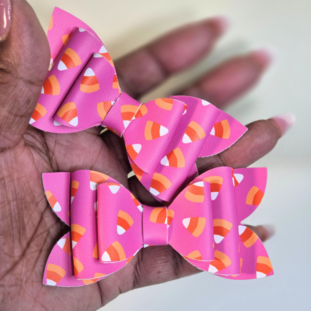 Two pink ribbon hair bows with a candy corn pattern, held in a person&