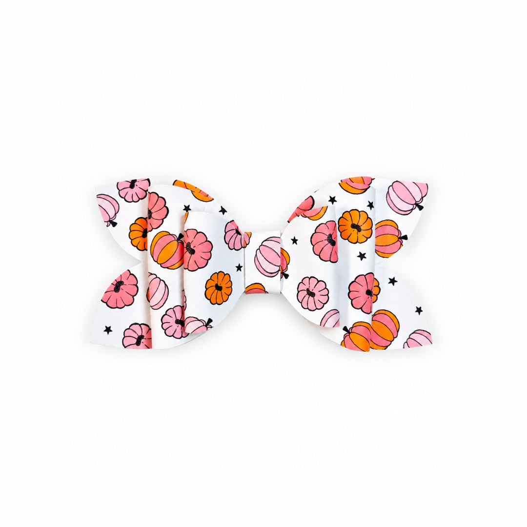 A white faux leather hair bow featuring a colorful pattern of pink and orange pumpkins, flowers, and small black stars, shown against a plain white background.
