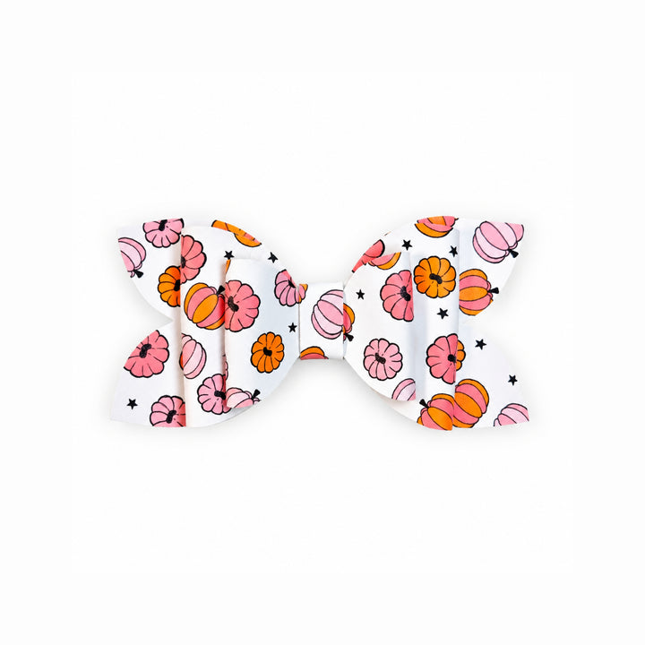 A white faux leather hair bow featuring a colorful pattern of pink and orange pumpkins, flowers, and small black stars, shown against a plain white background.