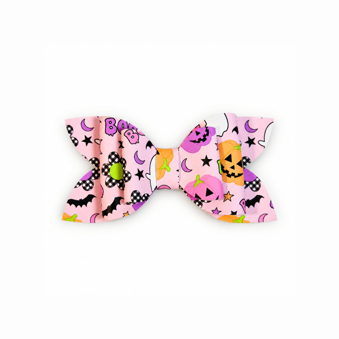 A faux leather hair bow featuring a colorful Halloween pattern with pumpkins, moons, stars, and the word 'BOO' on a light pink background.