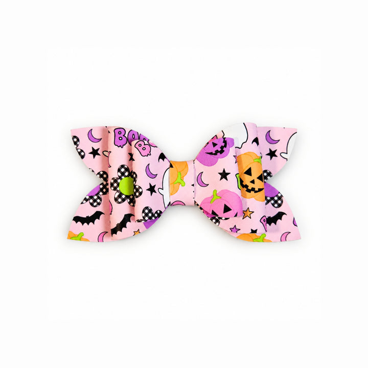 A faux leather hair bow featuring a colorful Halloween pattern with pumpkins, moons, stars, and the word &