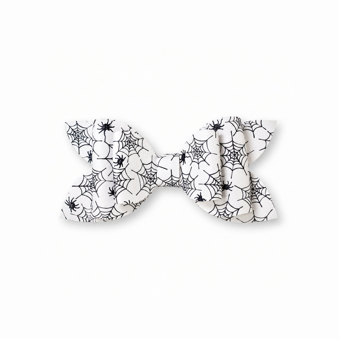 A white faux leather hair bow with a black spiderweb and spider print pattern, shown against a plain white background.