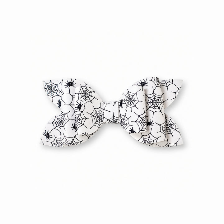 A white faux leather hair bow with a black spiderweb and spider print pattern, shown against a plain white background.